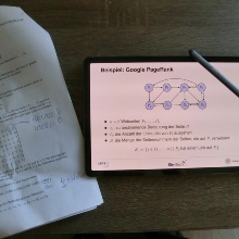 Schreibtisch von Professor Göddeke von oben. Darauf liegt ein Tablet, auf dem ein Skript zu sehen ist, und Arbeitsmaterial in Papierform.